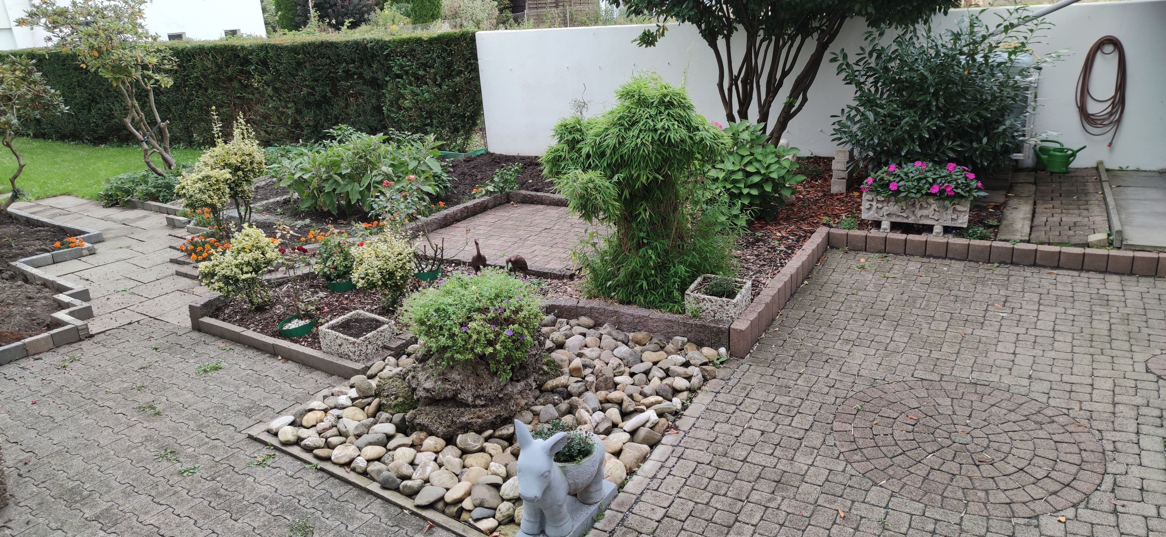 Un jardín con diversas plantas, un sendero de piedra y una pequeña estatua.