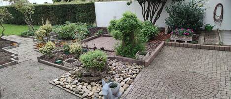 A garden with various plants, a stone pathway, and a small statue.
