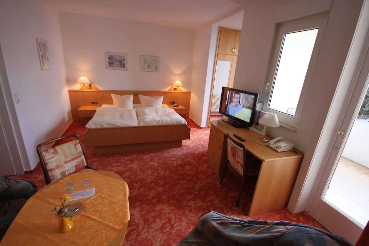 Een hotelkamer met een bed, bedlampen, een televisie, een bureau met telefoon, en een zithoek met tafel en stoelen.