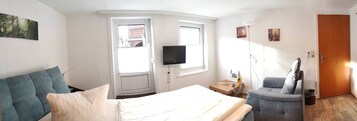 A hotel room with a bed, a sofa, a TV, and a wooden floor.