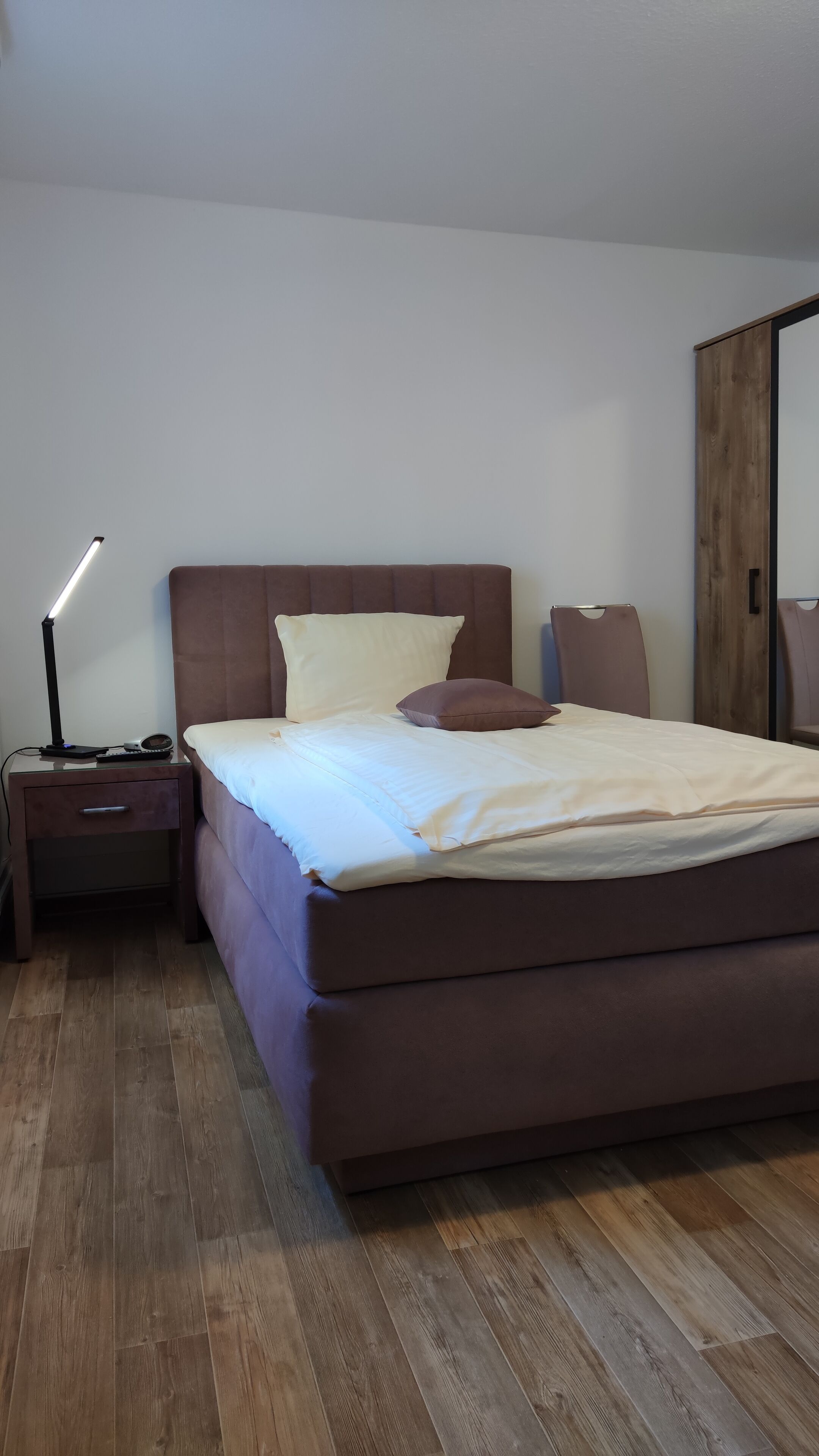 Un dormitorio con cama, mesita de noche, lámpara y suelo de madera.
