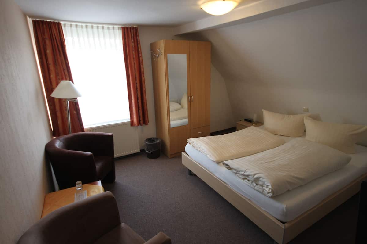 Een hotelkamer met een bed, bureau, stoel, kledingkast en raam met gordijnen.