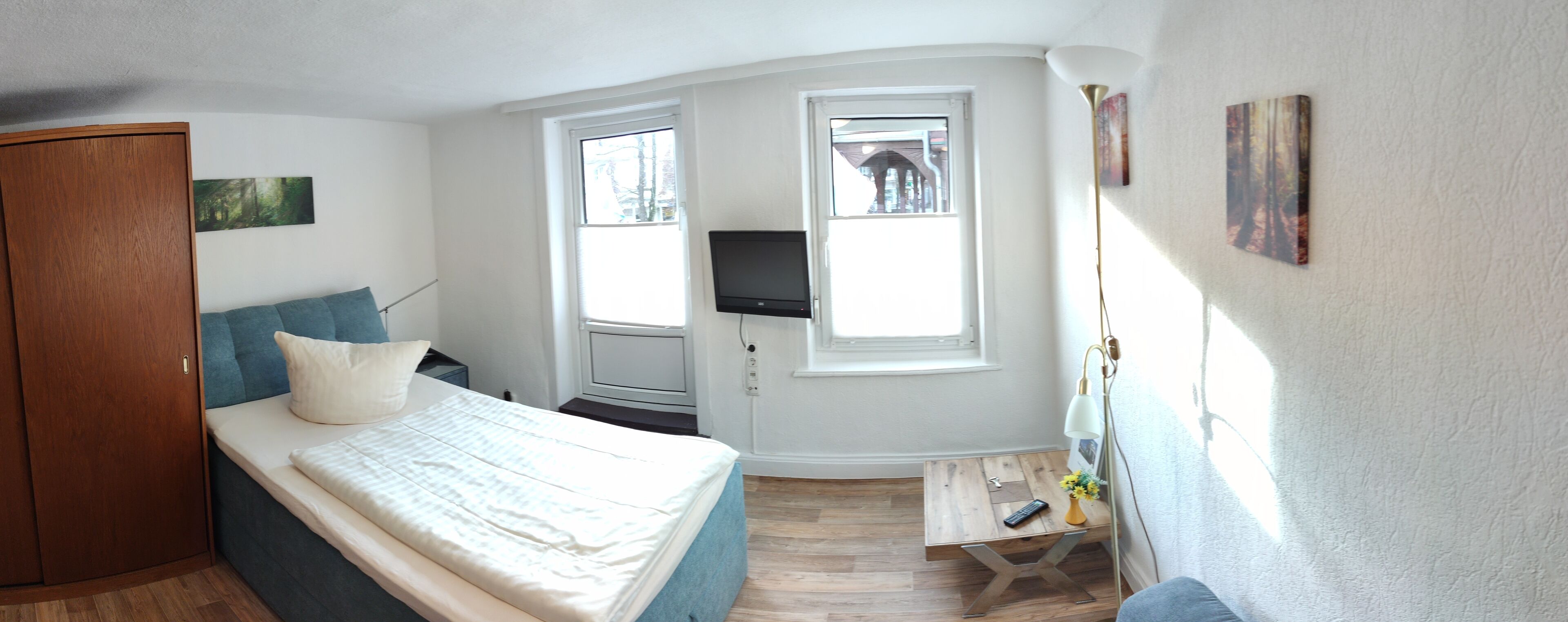 Un dormitorio con cama, armario, escritorio con lámpara, televisor y dos ventanas.