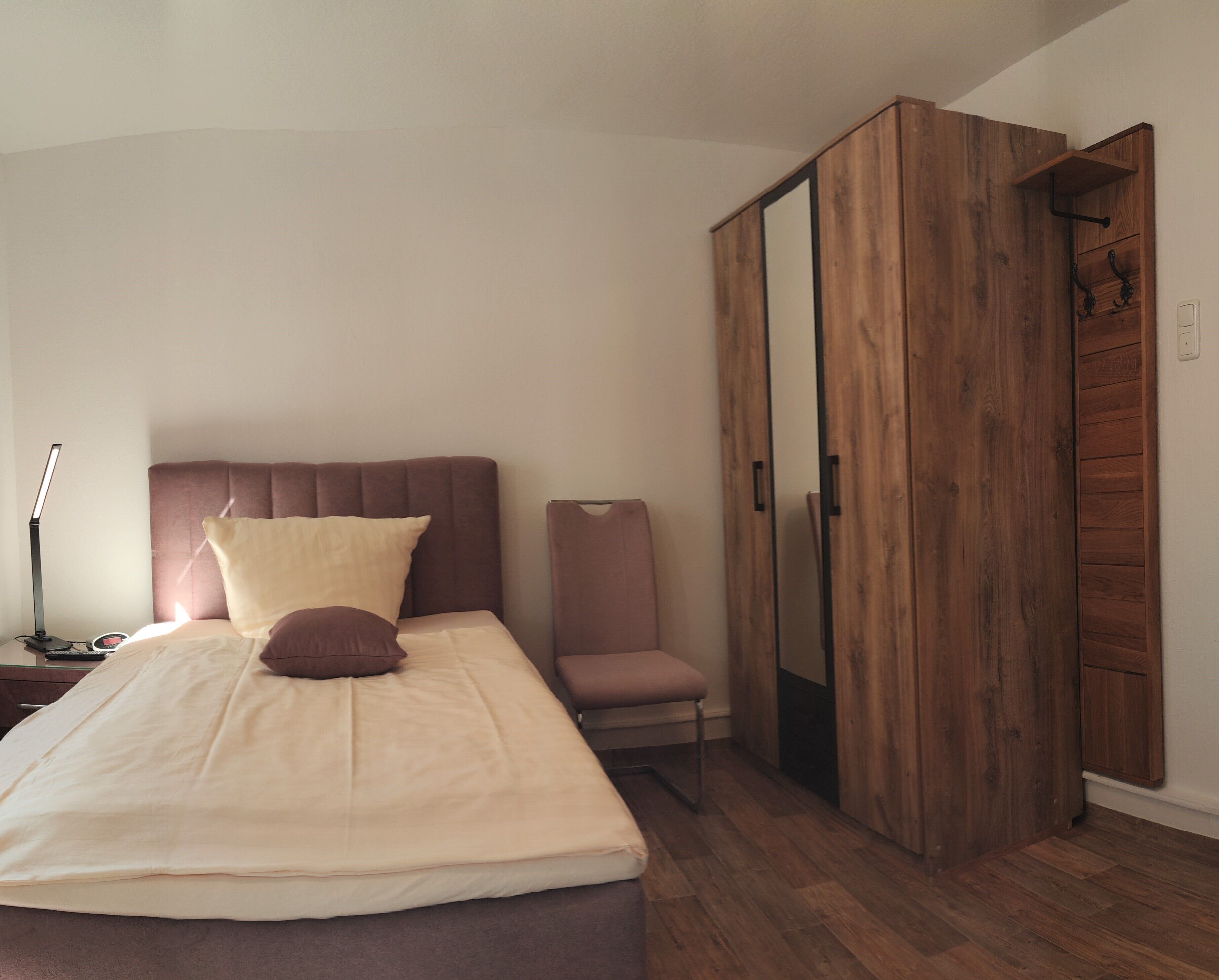 Een slaapkamer met een bed, nachtkastje, bureaulamp, stoel en een kledingkast.