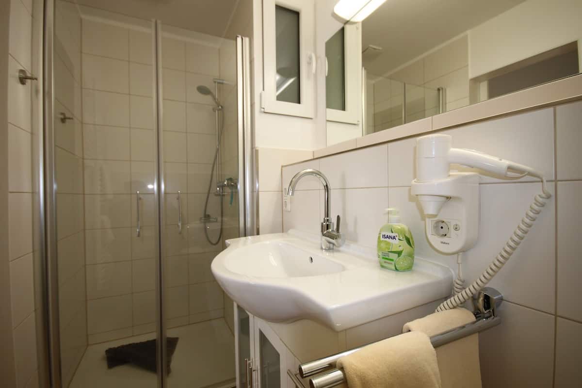 Een badkamer met een douche met glazen wand, een witte wastafel en een handdoekrek.