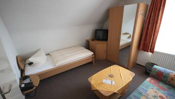 Ein kleines, kompaktes Zimmer mit einem Einzelbett, einem kleinen Tisch, einem Fernseher und einem Kleiderschrank.