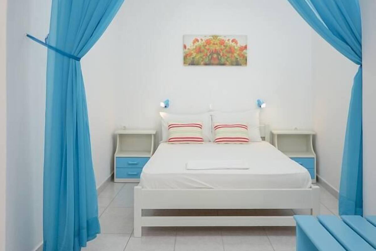 A bedroom with a bed, nightstands, a bench, and blue curtains.