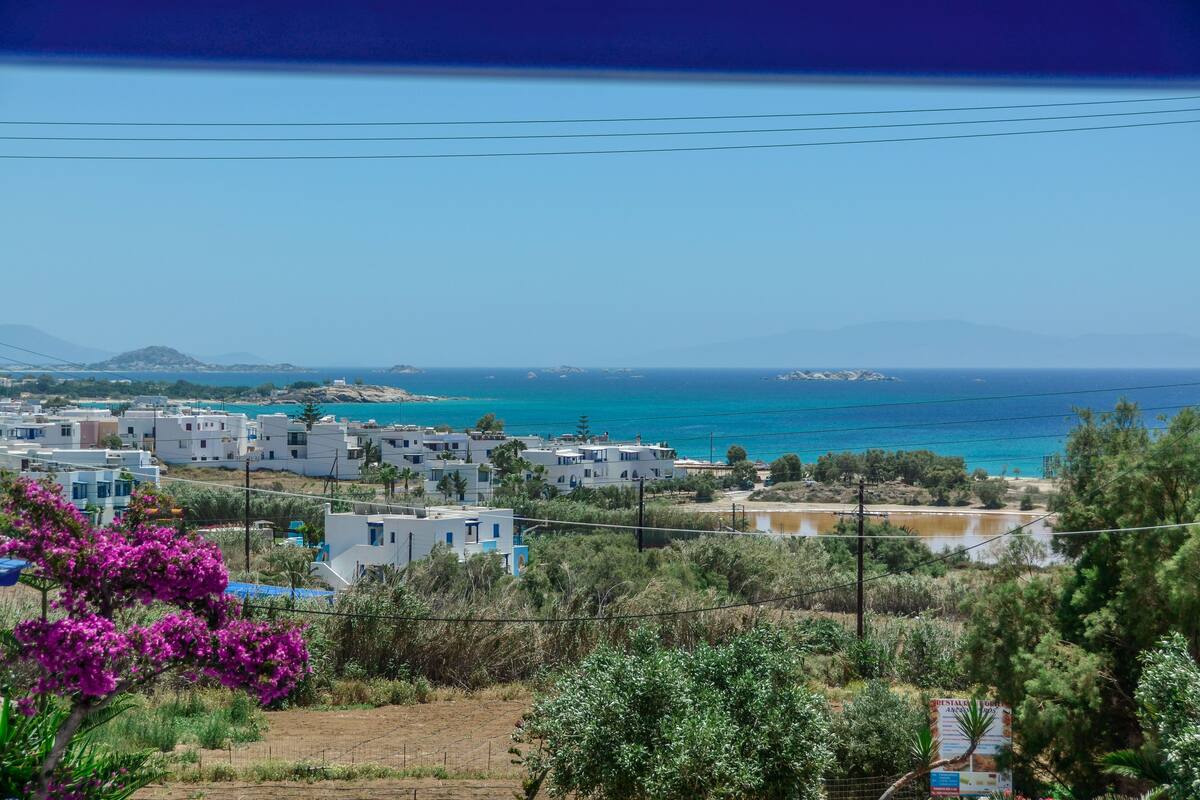 A coastal town with white buildings, a clear blue sea, and a distant mountain range.