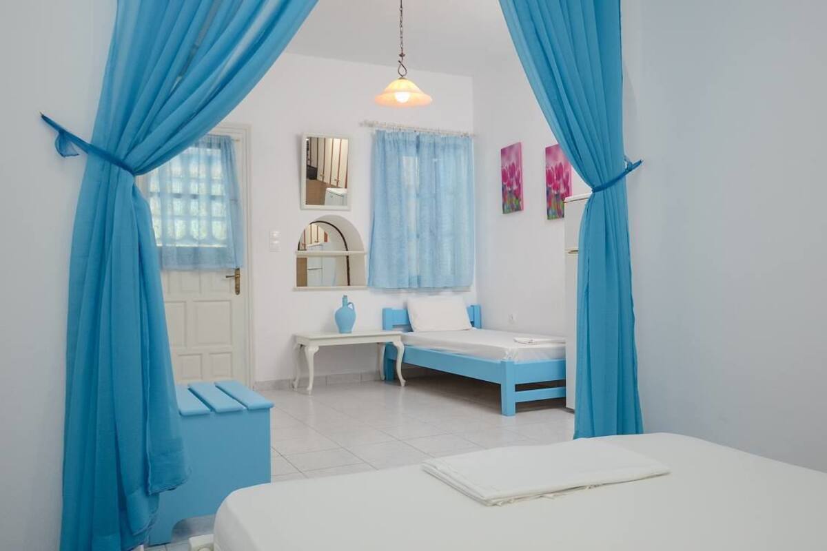 A bedroom with a bed, a bedside table, a mirror, a window with curtains, and a hanging light fixture.