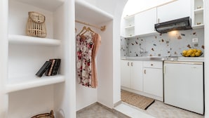 A modern kitchen with white cabinets, a black range hood, and a countertop with a bowl of fruit. - Studios Tasia (Naxos)