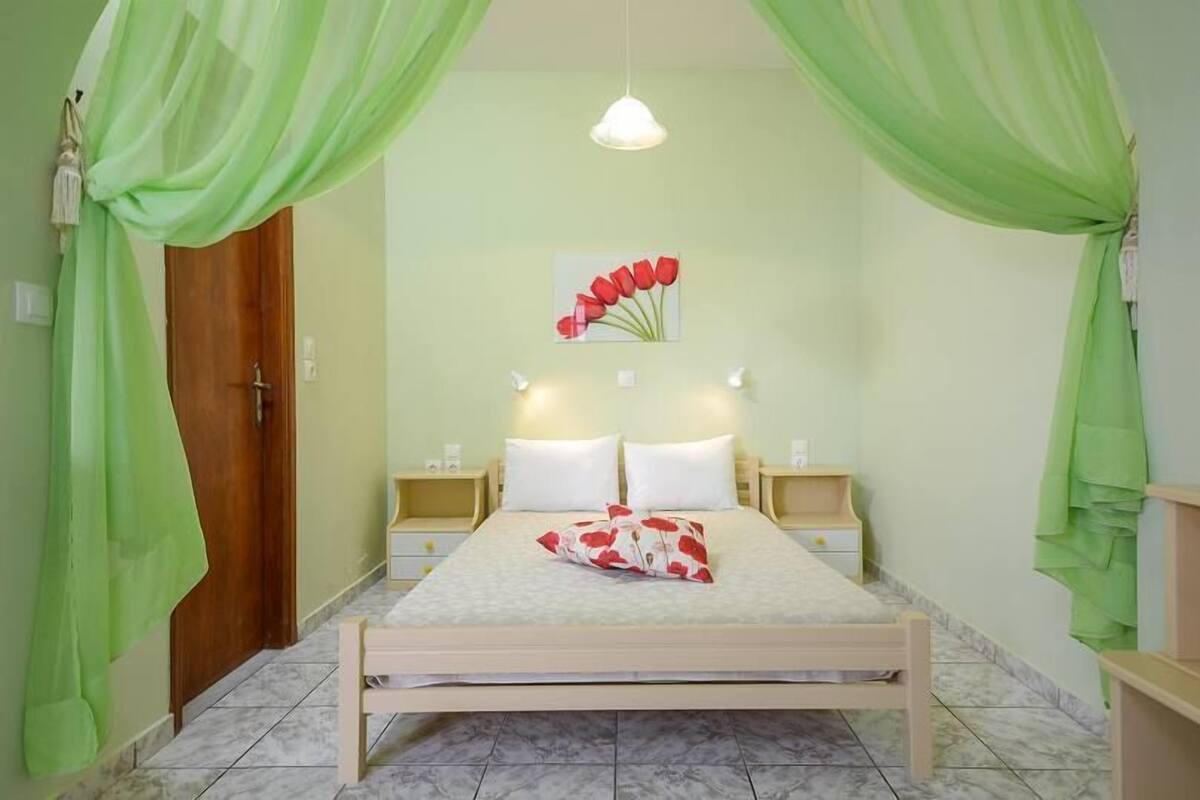 A bedroom with a bed, nightstands, a wooden door, and green curtains.