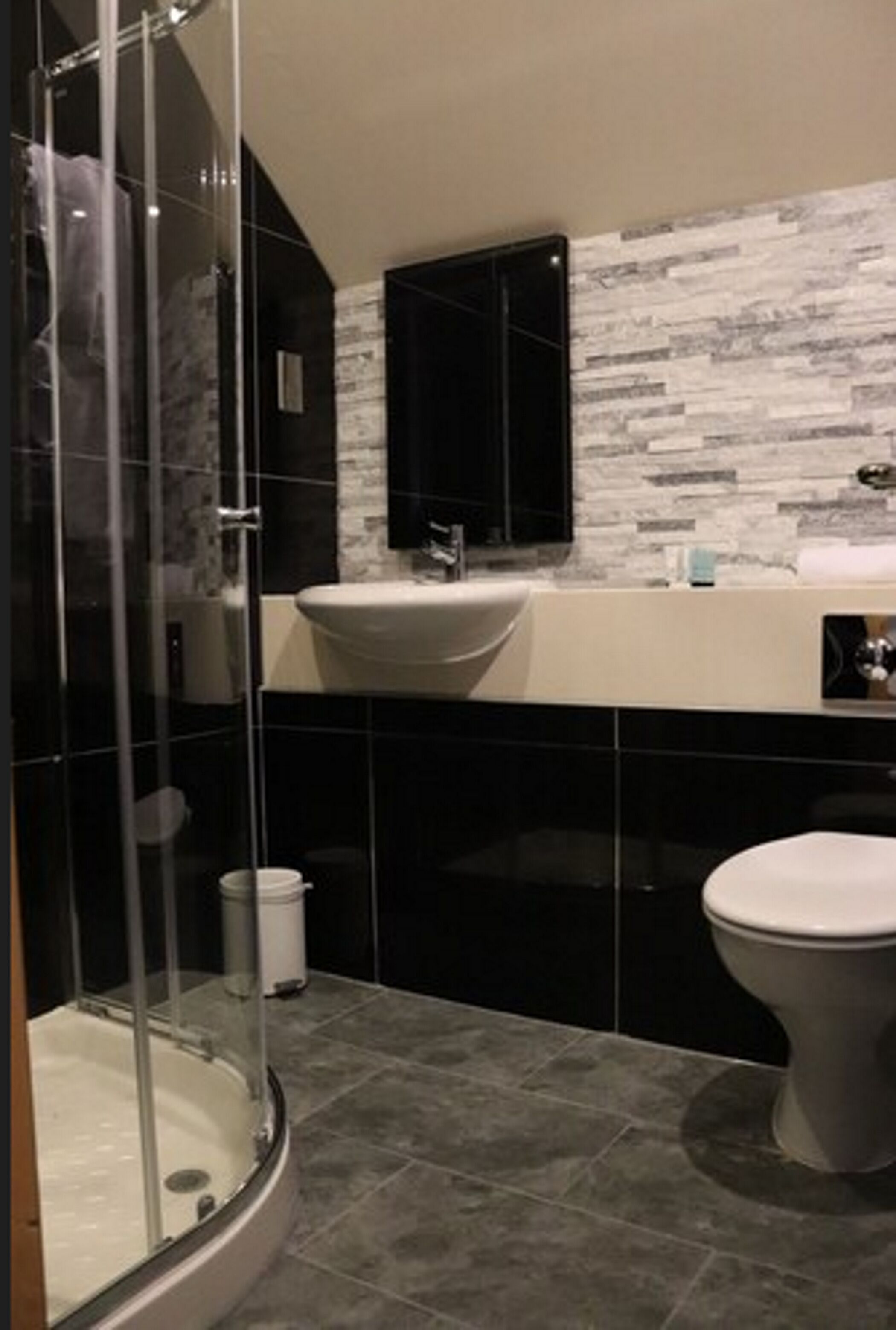 A modern bathroom with a glass-enclosed shower, a white sink, and a black toilet.