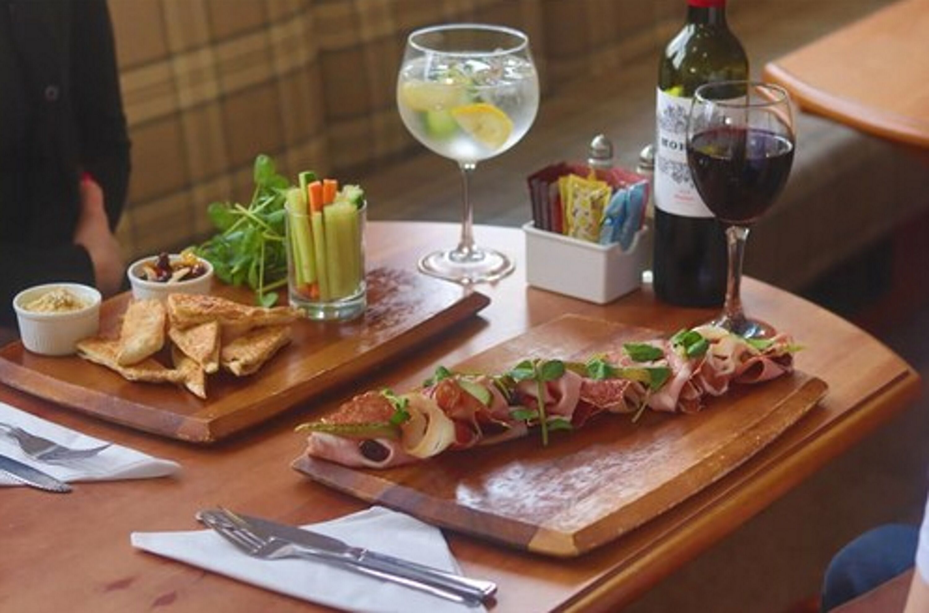 A table with a variety of food items, including a long piece of meat, a glass of red wine, and a glass of water with lemon slices.