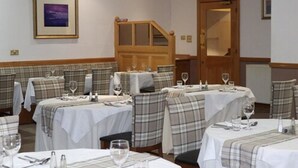 A dining area with tables set for two, each with plaid tablecloths and matching chairs. There is a wooden door in the background, and a framed picture on the wall. - Loch Long Hotel (Arrochar)