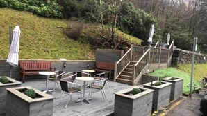An outdoor patio with wooden furniture, a staircase, and a stone wall. - Loch Long Hotel (Arrochar)