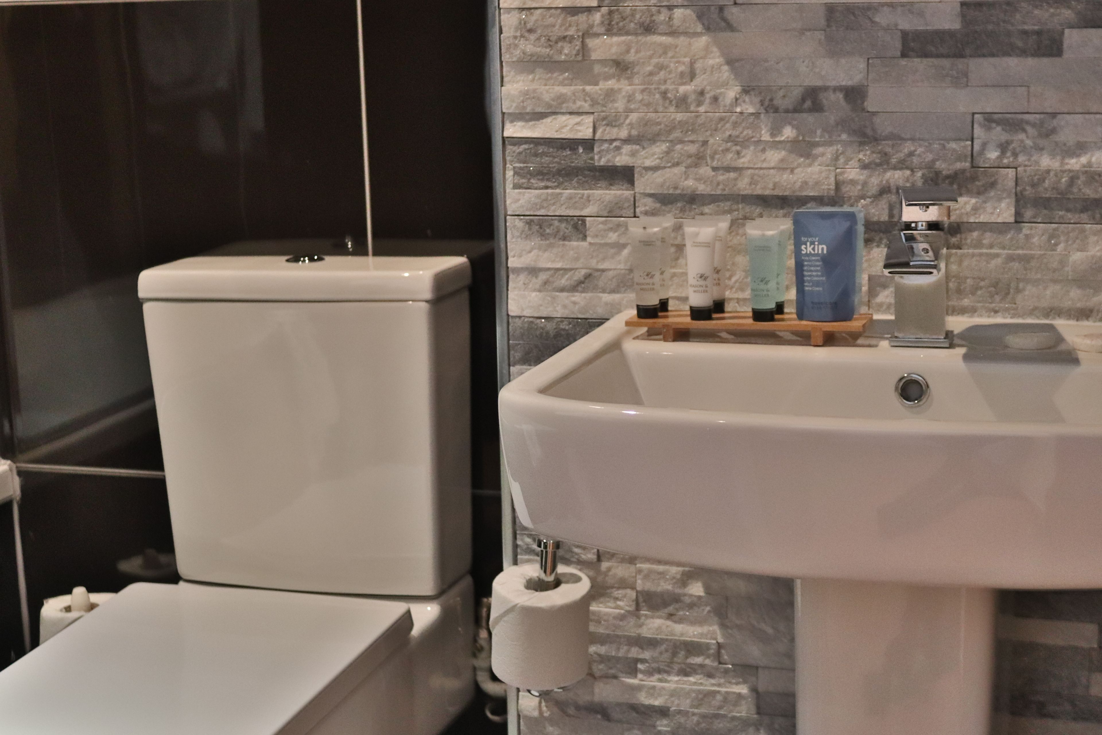 A bathroom with a toilet, a sink, and toiletries on a shelf.