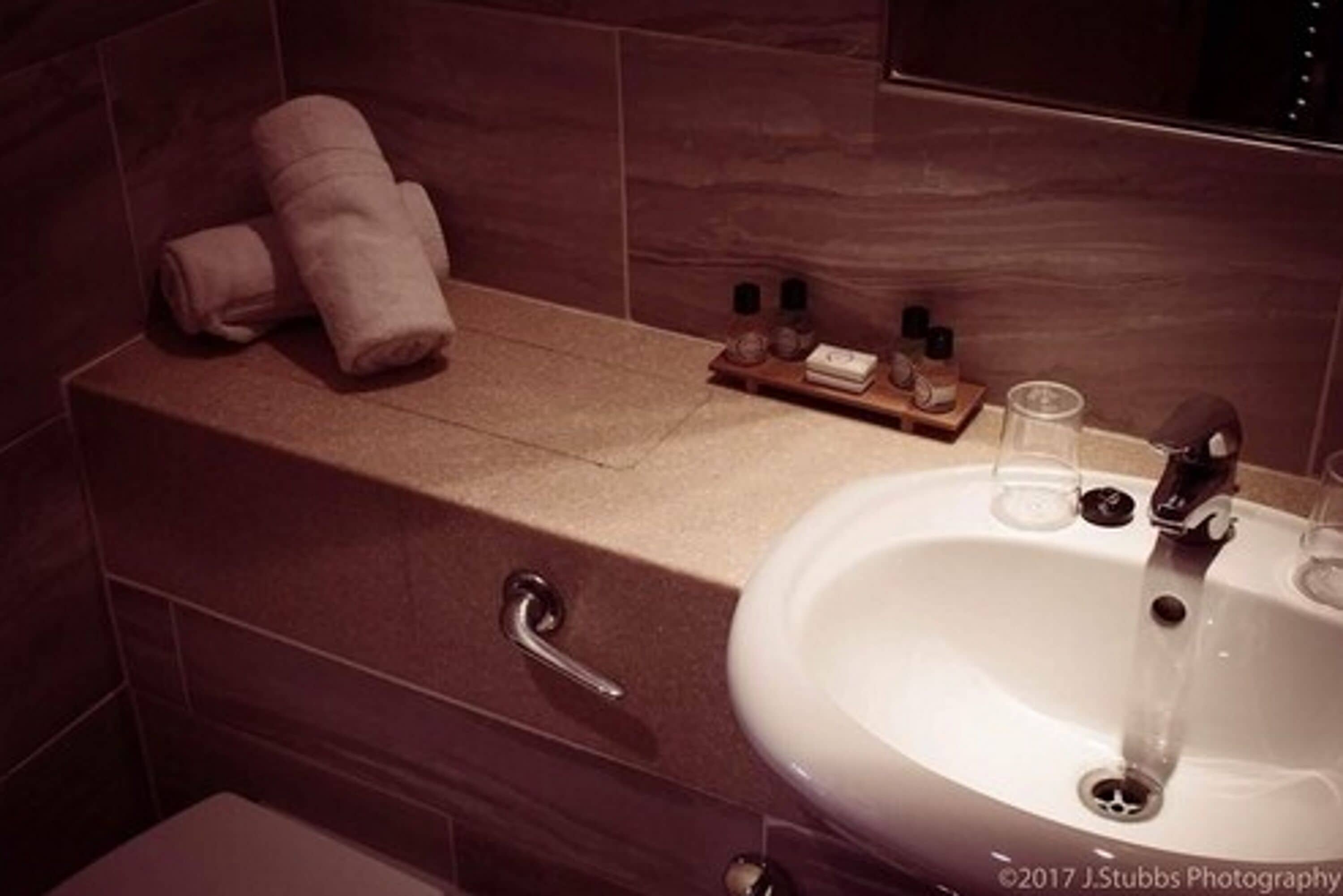 A bathroom with a white sink, a towel rack with towels, and a shelf with toiletries.