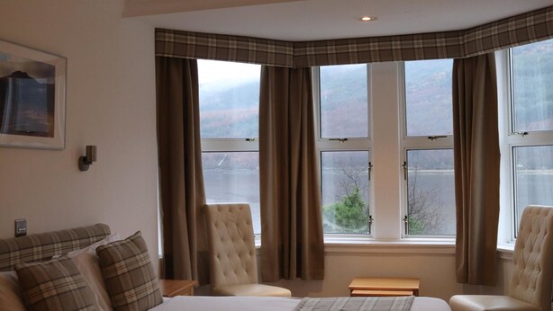 A hotel room with a bed, two armchairs, a small table, and a window with curtains. - Loch Long Hotel (Arrochar)