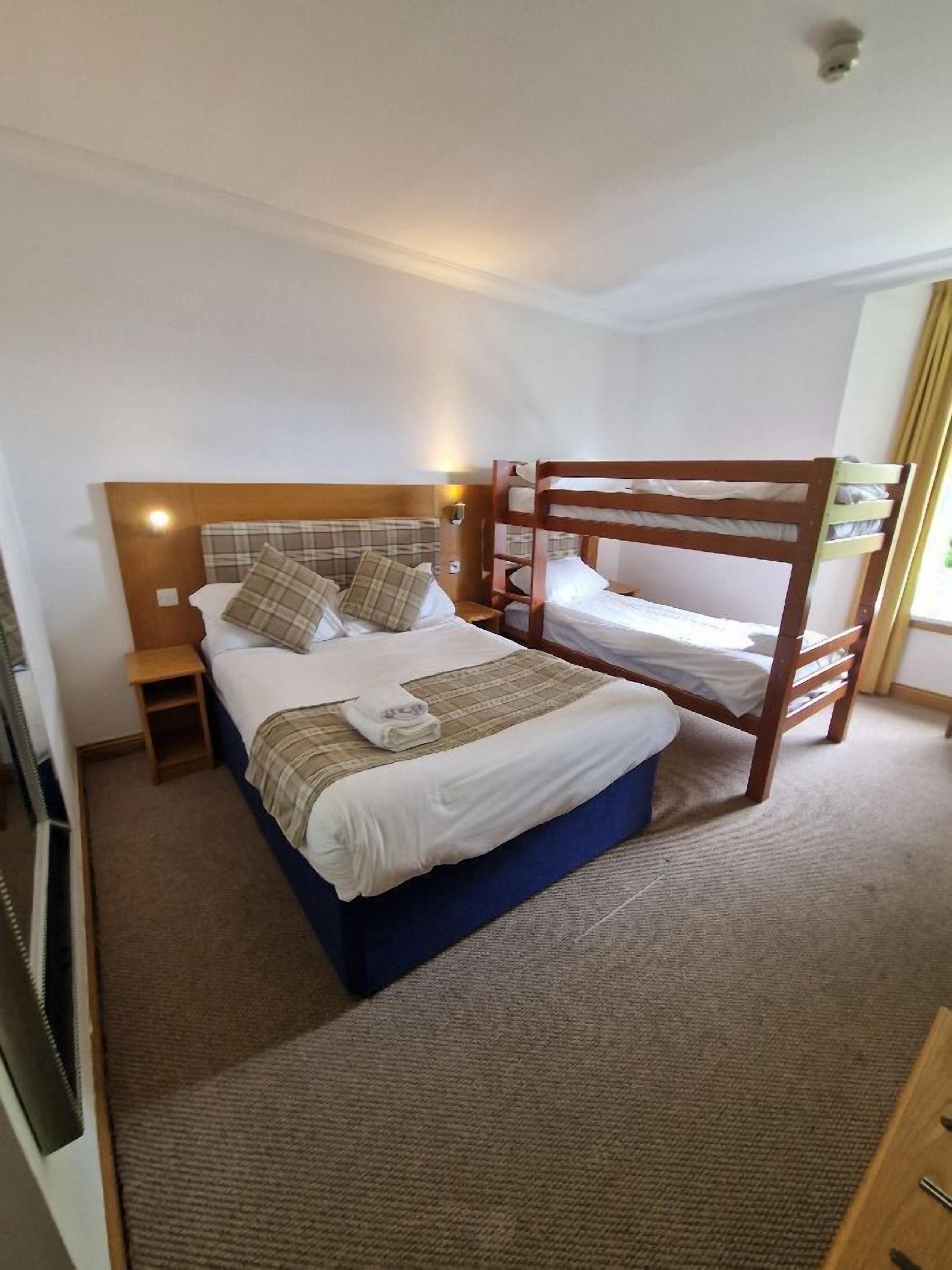 A double bed with a wooden headboard and footboard, a bedside table, and a wall-mounted light.