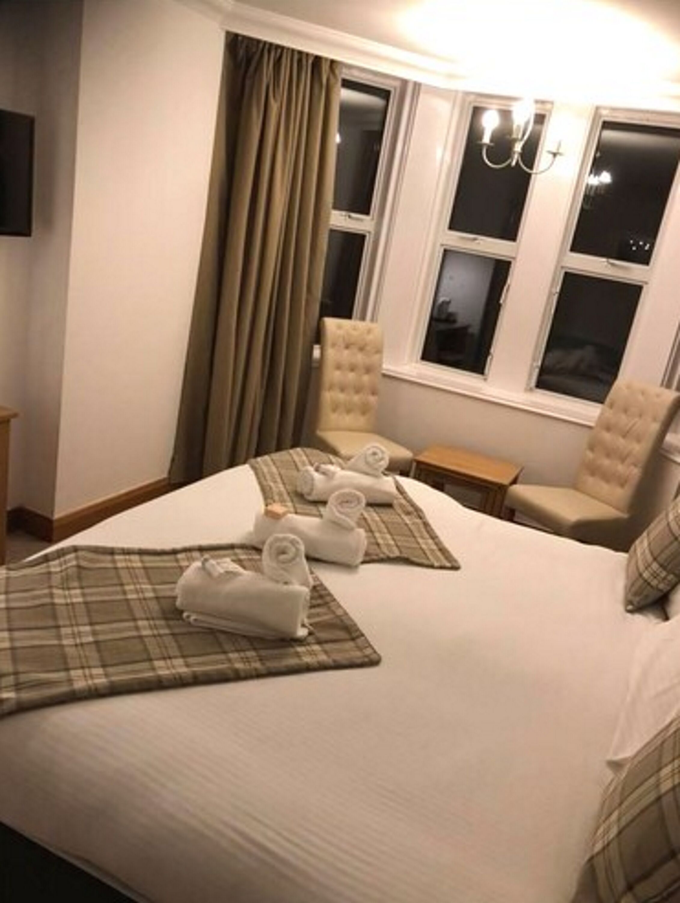 A hotel room with a bed, two armchairs, a nightstand, and a window with curtains.