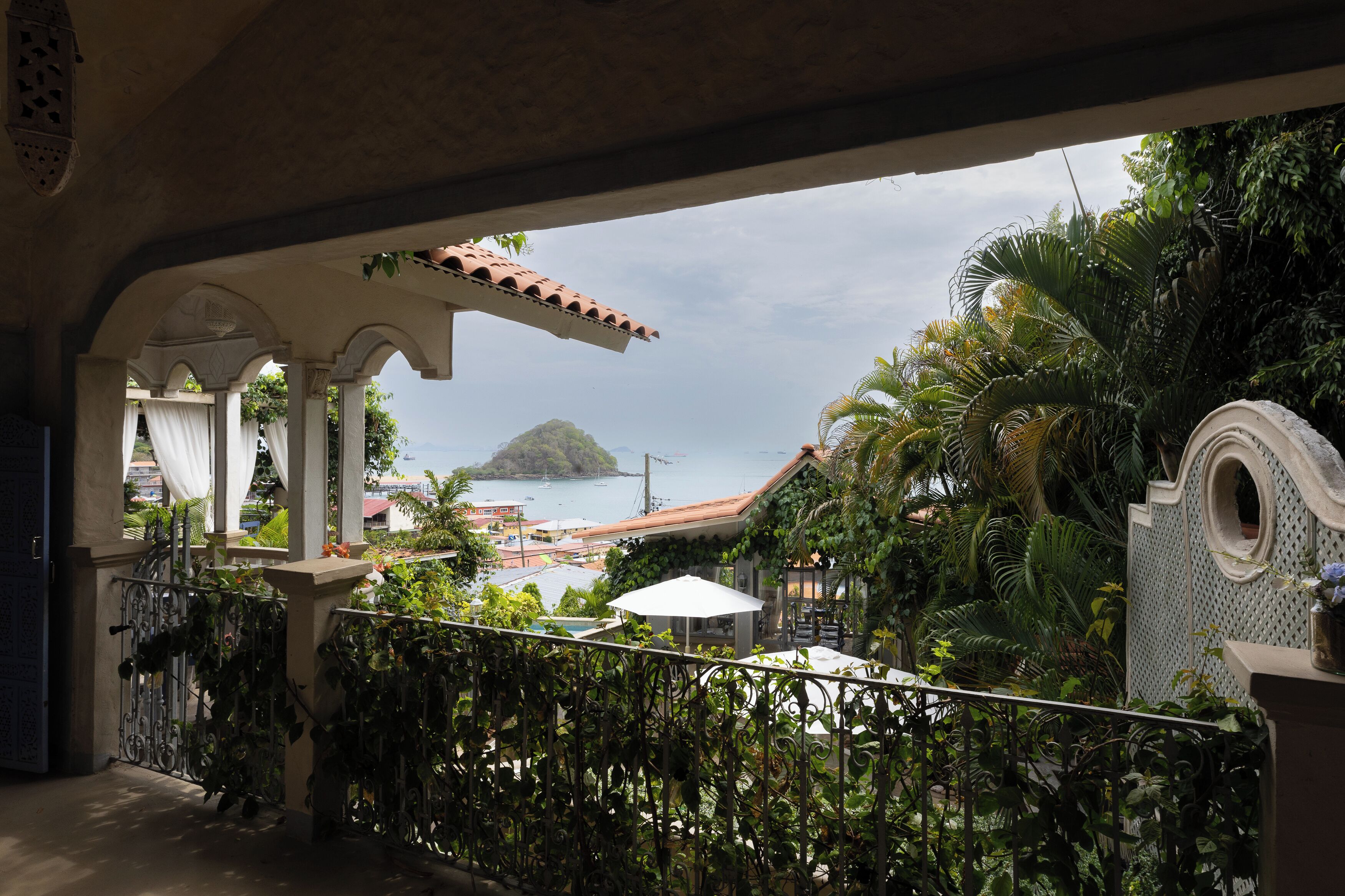 A balcony with a view of a tropical island, lush greenery, and a clear sky.