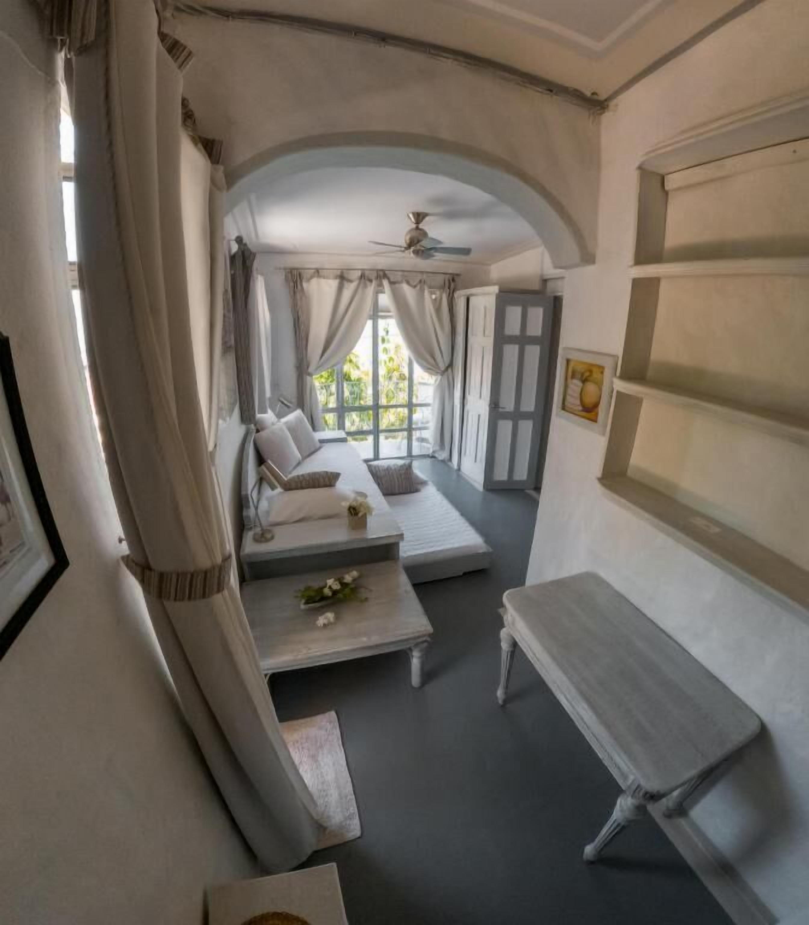 A cozy room with a bed, a small table, and a bench. There is a window with curtains and a door leading outside.