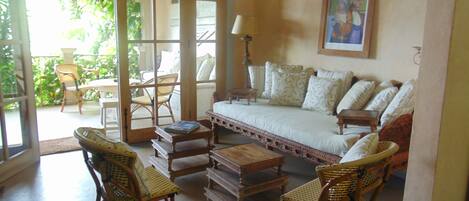 A cozy living room with a sofa, two wicker chairs, a coffee table, and a bookshelf.