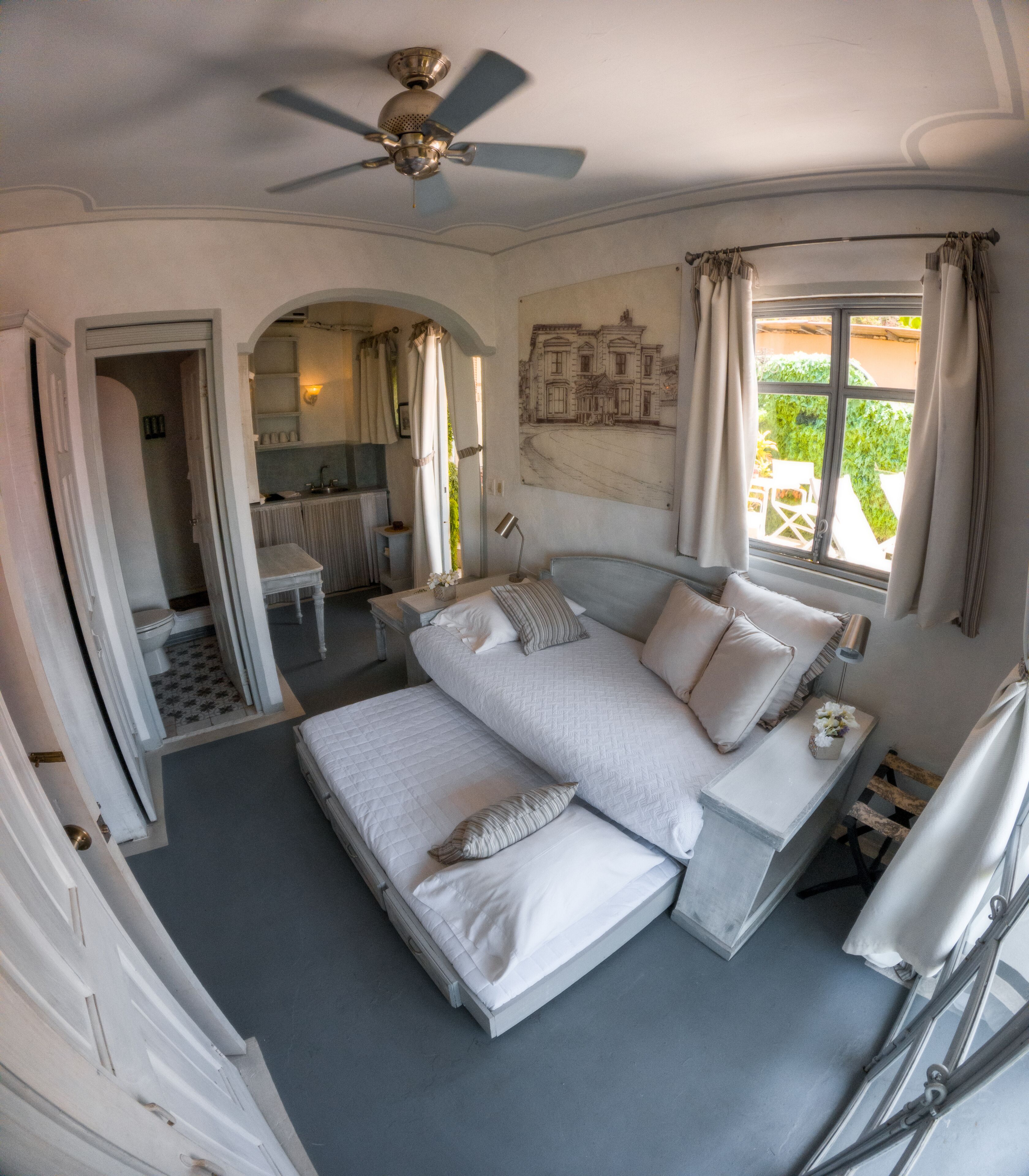 A bedroom with a double bed, a ceiling fan, and a view of the garden through a window.