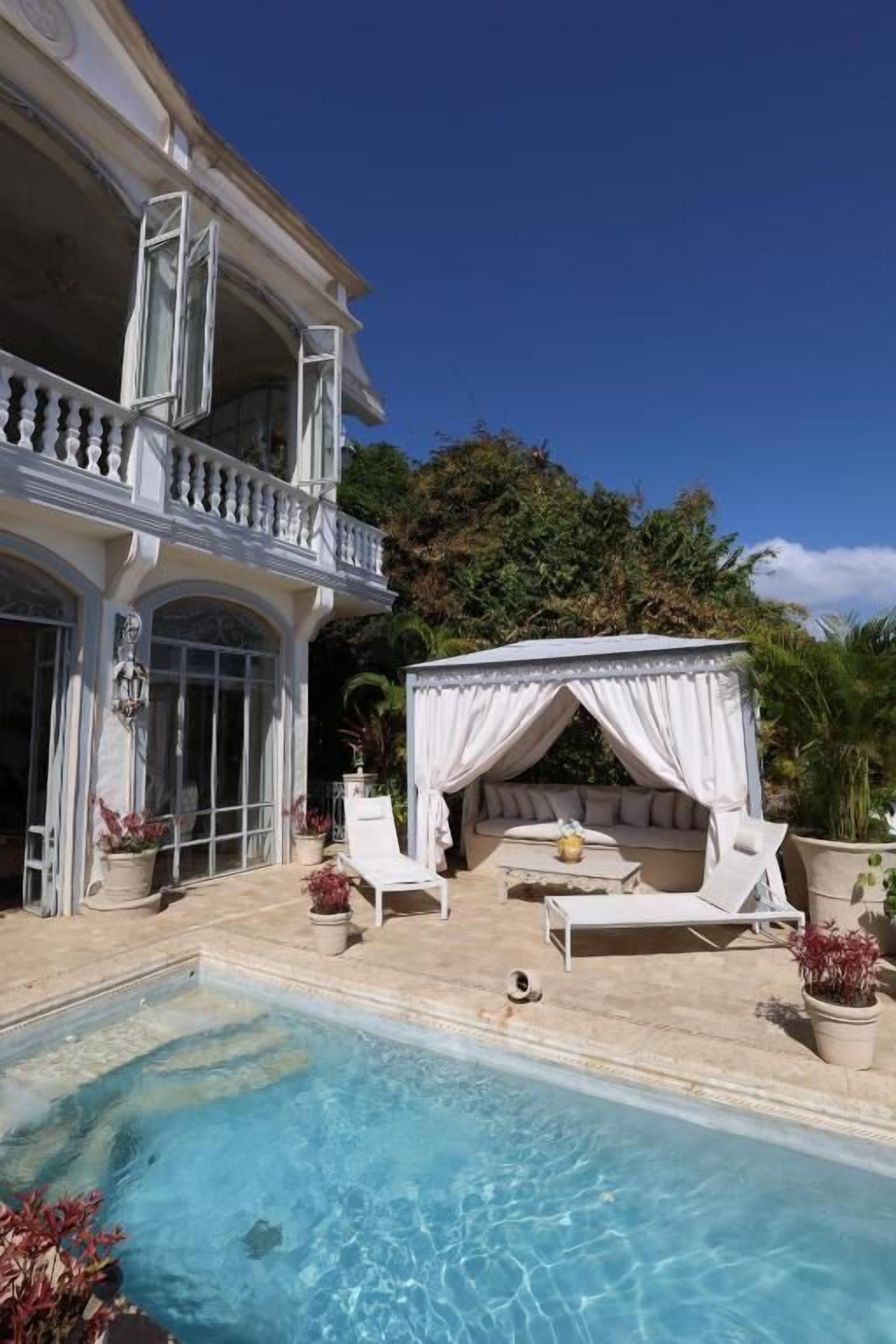A poolside area with a white outdoor seating area, a covered seating area, and a pool.
