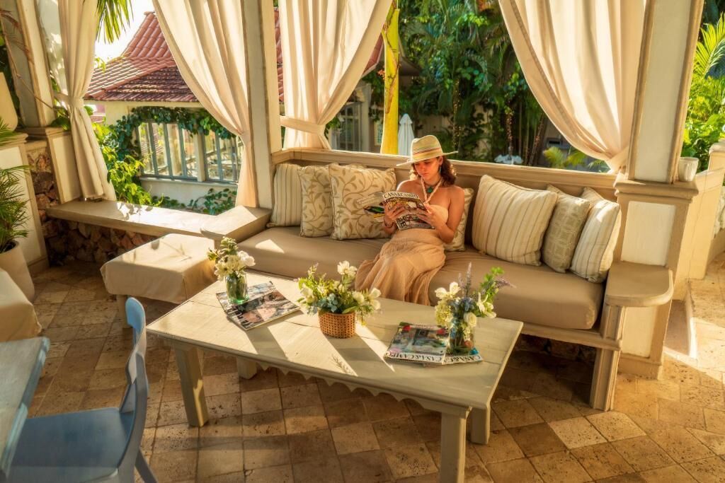Ein gemütlicher Sitzbereich im Freien mit einer Couch, einem Tisch mit Zeitschriften und Blumen sowie Blick auf Grünflächen und ein Gebäude im Hintergrund.