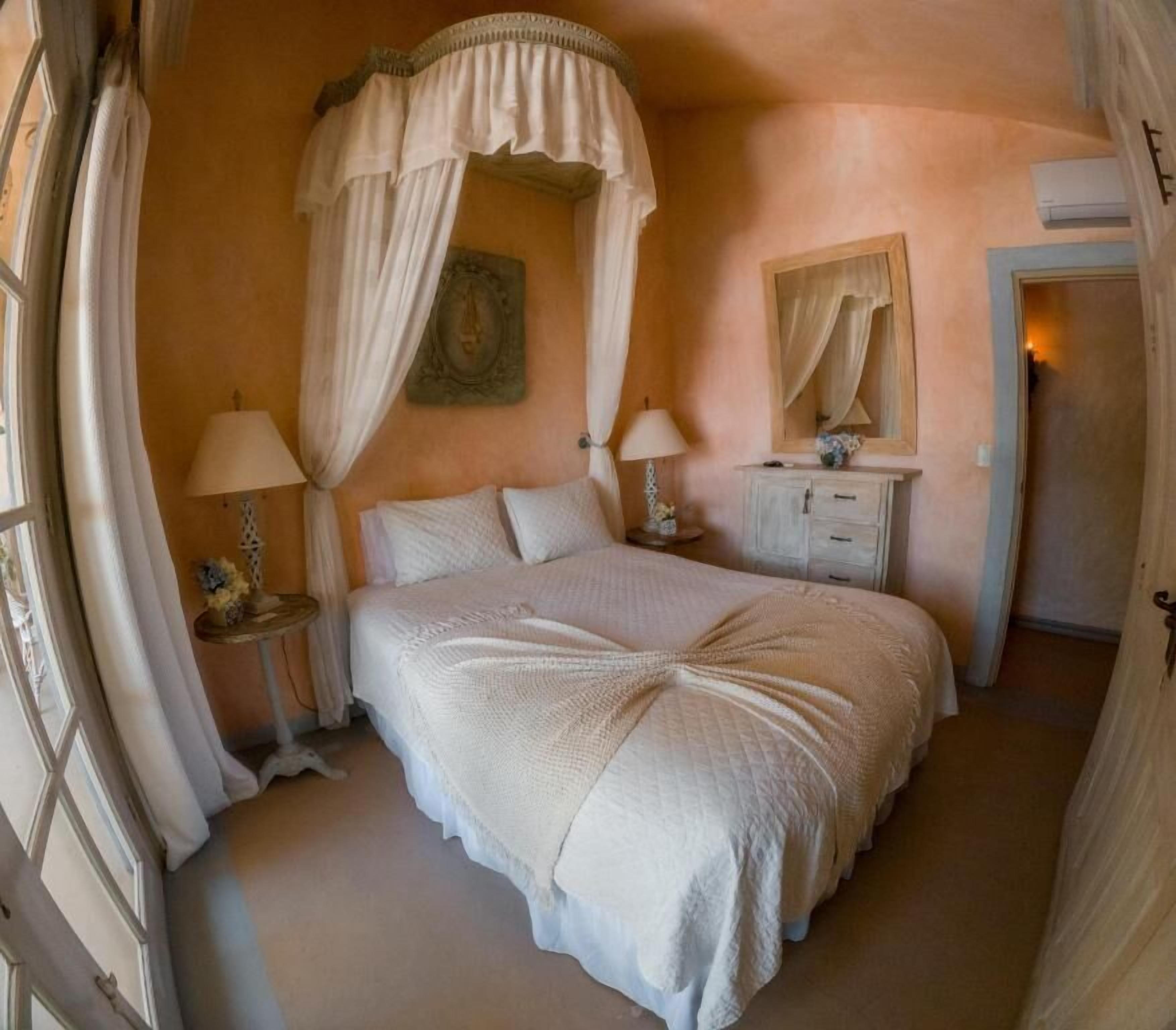 Un dormitorio con una cama con dosel, dos mesitas de noche con lámparas, un tocador y un espejo.