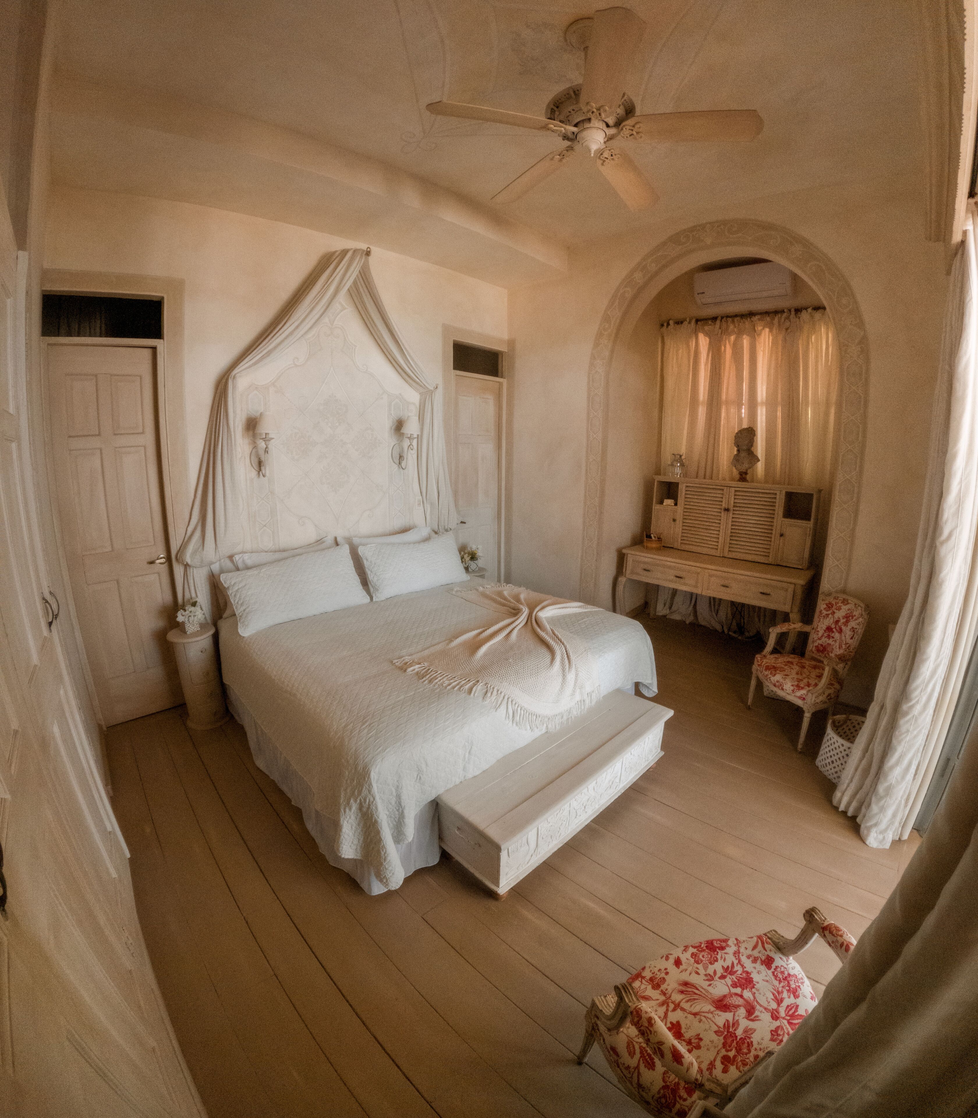 A bedroom with a large bed, a nightstand, a chair, and a vanity with a mirror.