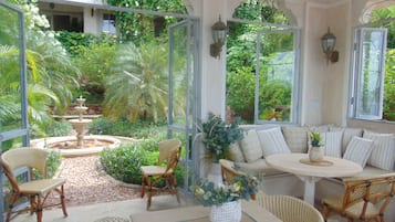 Ein Wintergarten mit Sitzgelegenheit, einem Springbrunnen und üppiger Bepflanzung.