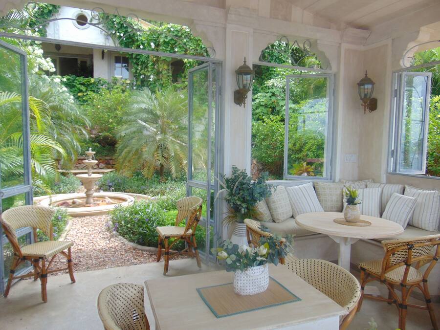 Ein Wintergarten mit Sitzgelegenheit, einem Springbrunnen und üppiger Bepflanzung.