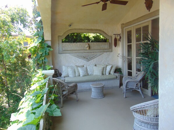 A sunlit patio with a cushioned seating area, wicker chairs, and a ceiling fan. - Villa Caprichosa (Taboga)