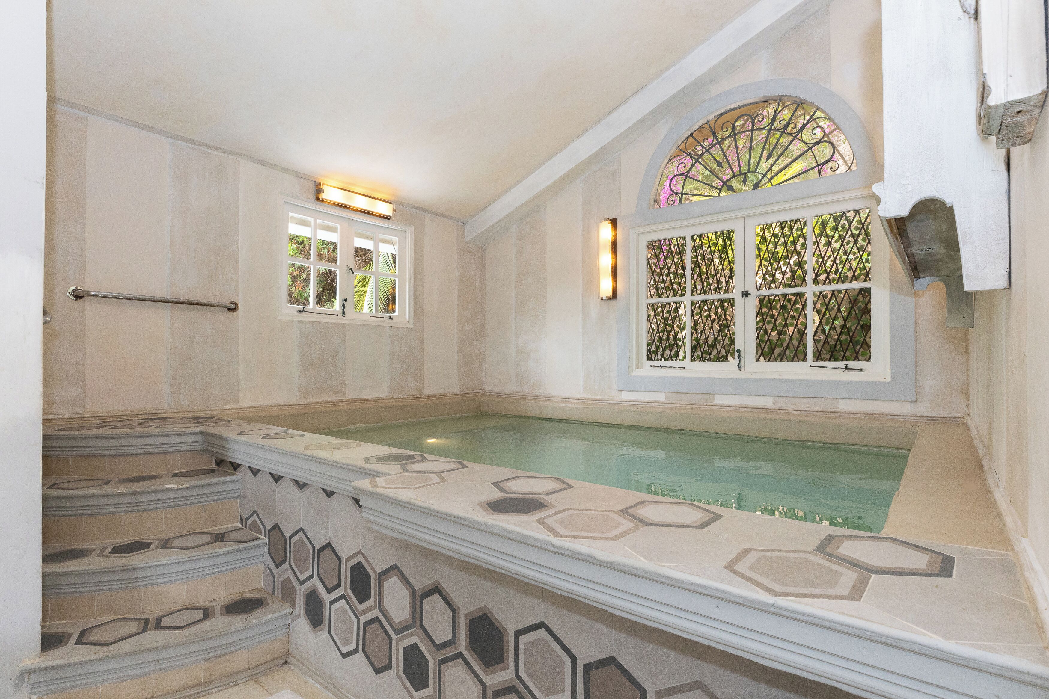A bathroom with a hexagonal tile design, a bathtub, and a window with a decorative grille.