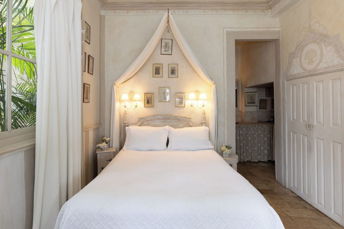 Ein großes Bett mit Baldachin, gerahmte Bilder an der Wand und ein kleiner Tisch mit Blumenvase.