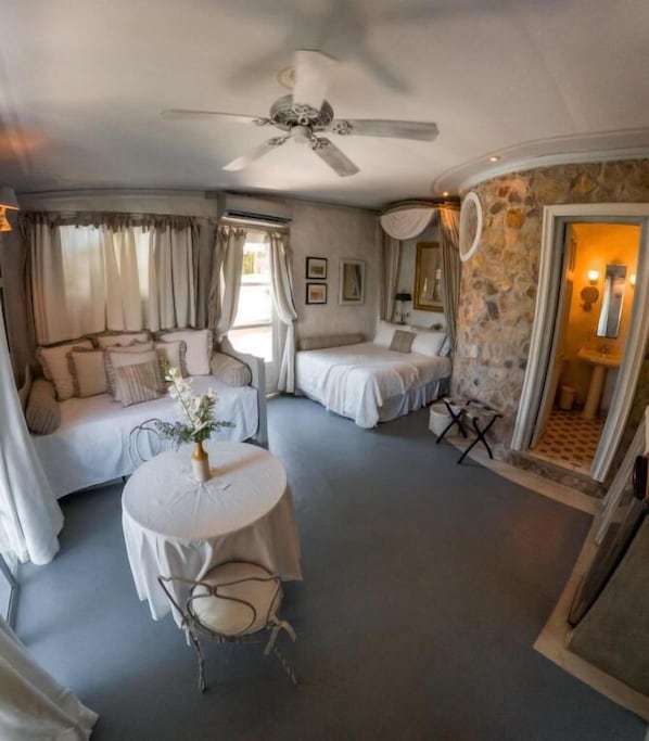 A hotel room with a bed, a smaller bed, a round table with a chair, and a ceiling fan. - Villa Caprichosa (Taboga)