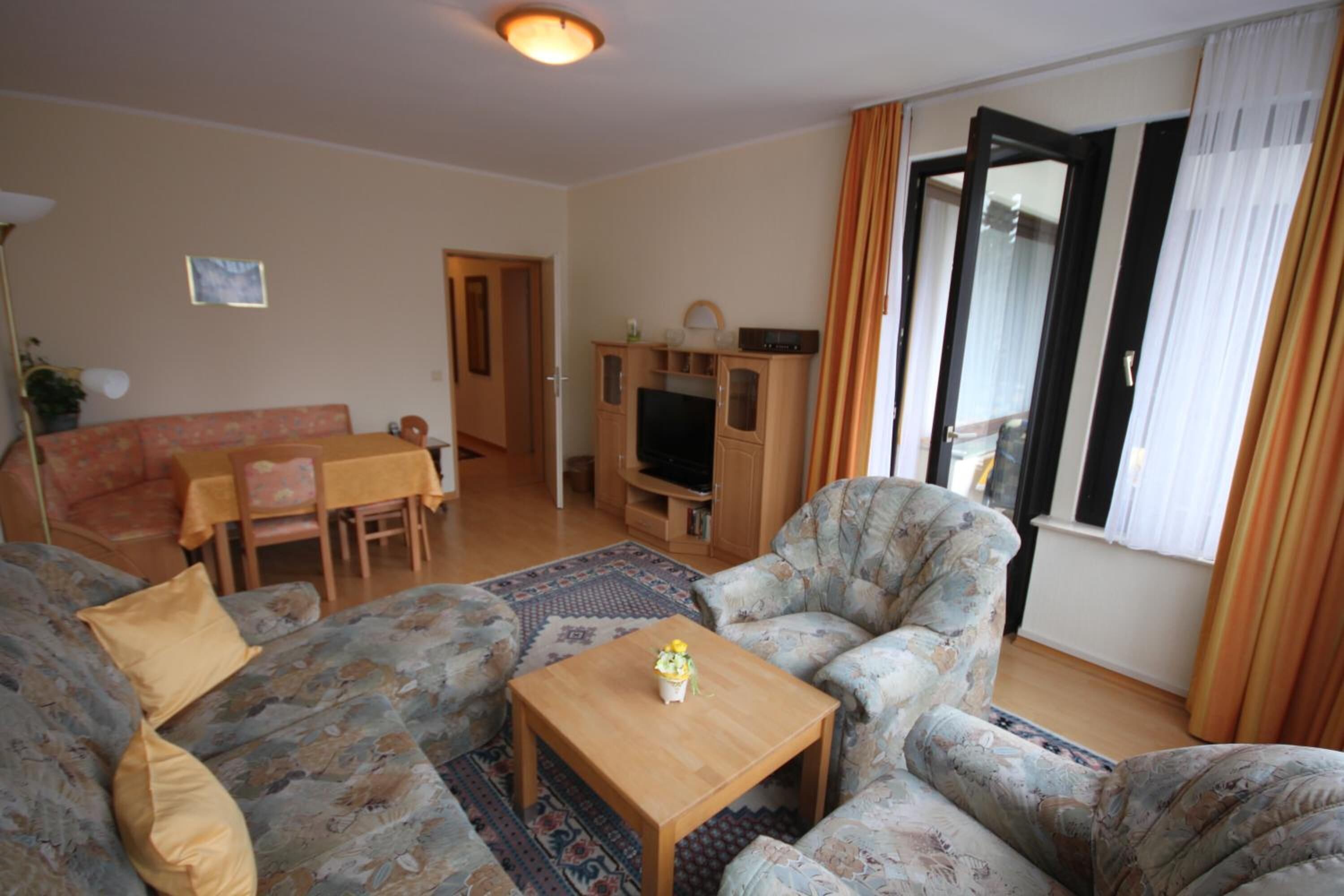 Ein Wohnzimmer mit einer Couch, Sesseln, einem Couchtisch, einem Fernseher und einem Essbereich mit Tisch und Stühlen.