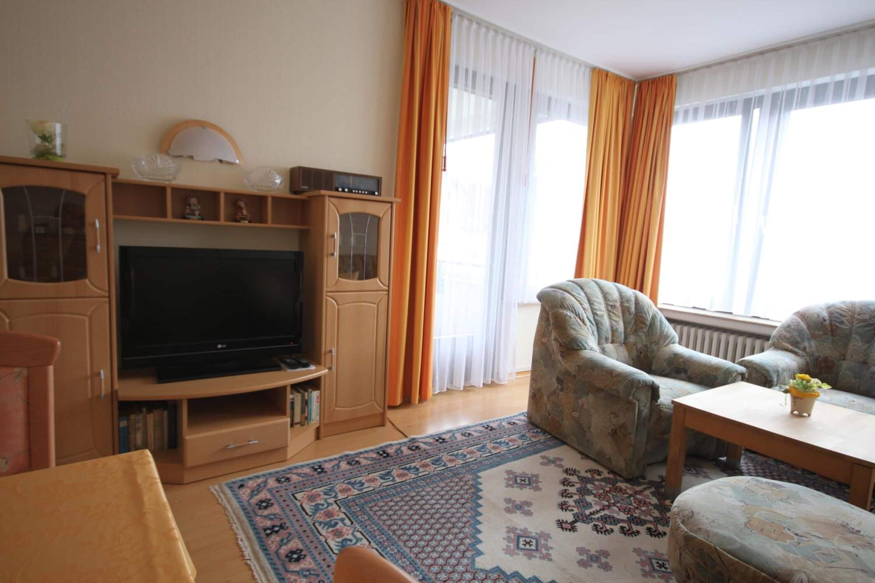Ein Wohnzimmer mit Fernseher, Sofa, Sessel und einem gemusterten Teppich.