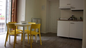 A dining area with a white table and yellow chairs, a kitchen with white cabinets, and a door leading to another room. - Il Conservatorio B&B (Naples)