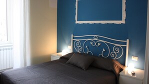 A bedroom with a bed, white nightstands, a wall-mounted light, and a window with curtains. - Il Conservatorio B&B (Naples)