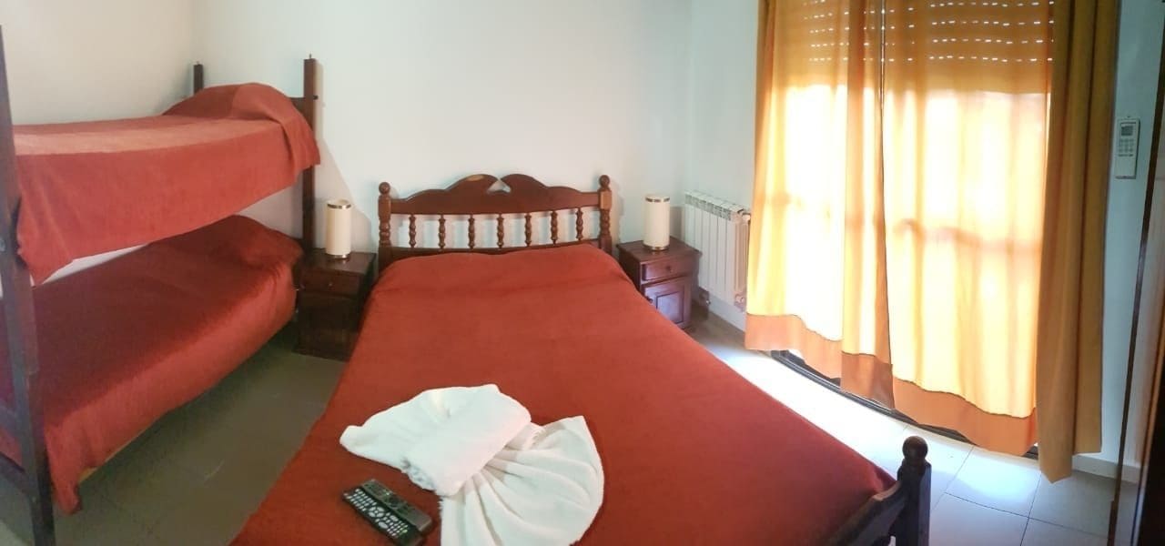 A room with a bunk bed, a single bed, a bedside table with a lamp, and a window with curtains.
