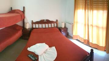 A room with a bunk bed, a single bed, a bedside table with a lamp, and a window with curtains.
