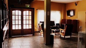 A living room with a sofa, chairs, a television, and a large window with curtains. - Departamentos Campitelli (General Pacheco)