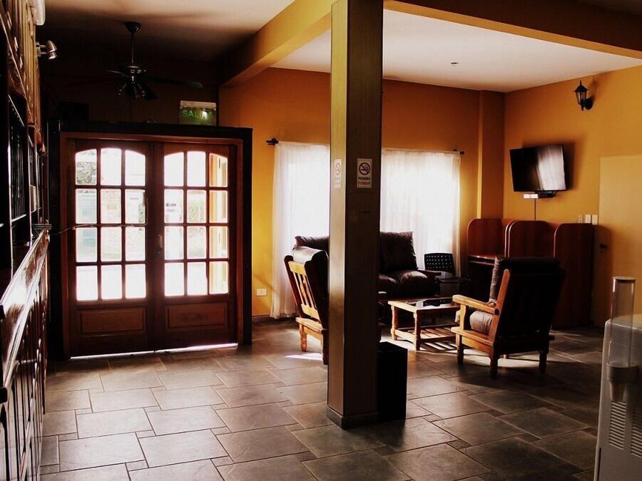 Una sala de estar con sofá, sillas, televisión y un ventanal con cortinas.