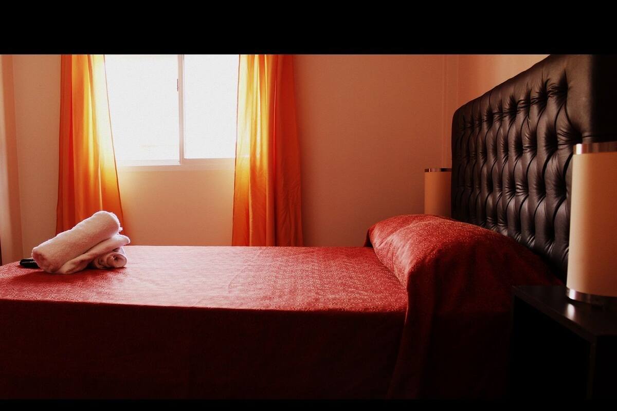 A hotel room with a bed, a nightstand, a lamp, and a window with curtains.