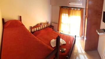 A single bed with a wooden frame and a red bedspread in a room with a window, a wall-mounted TV, and a radiator.