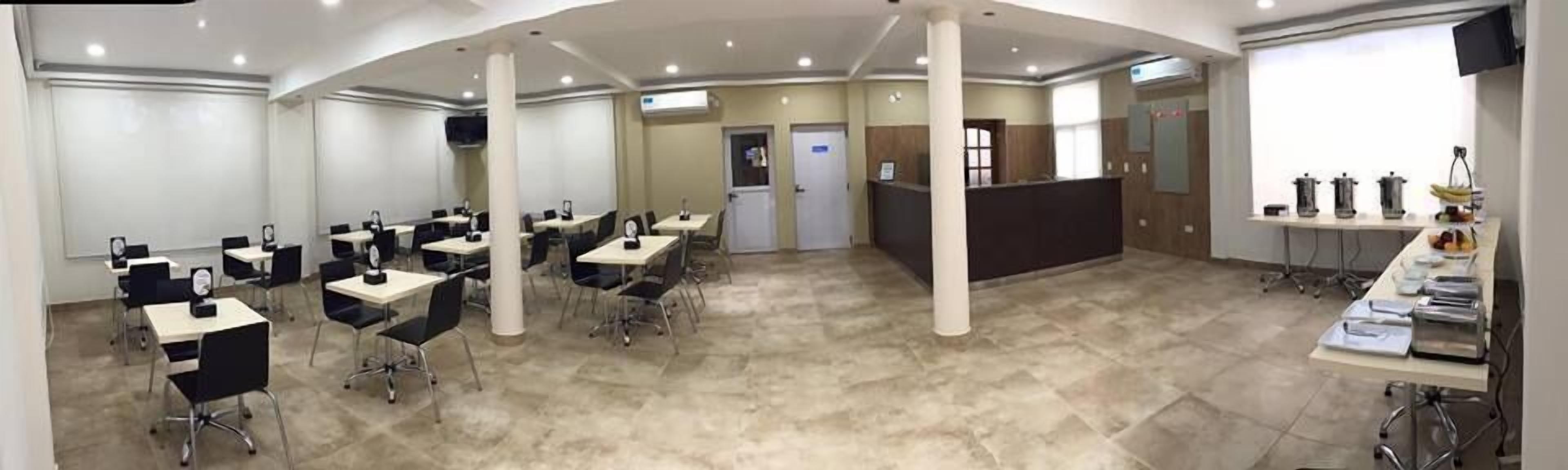 Una sala de conferencias con varias mesas y sillas, un mostrador de recepción y una zona de kitchenette.