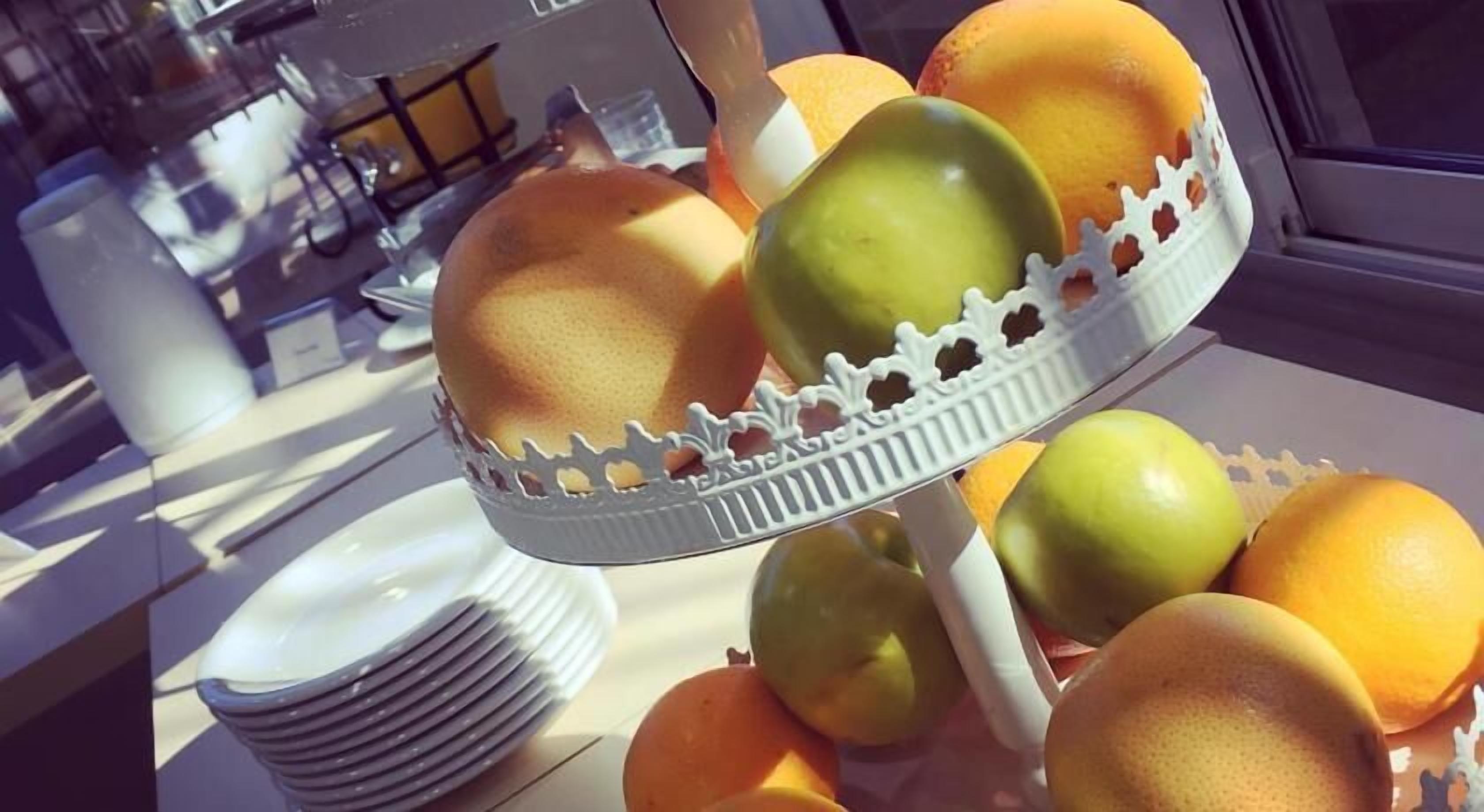 Una cesta de frutas con naranjas y manzanas sobre una mesa.